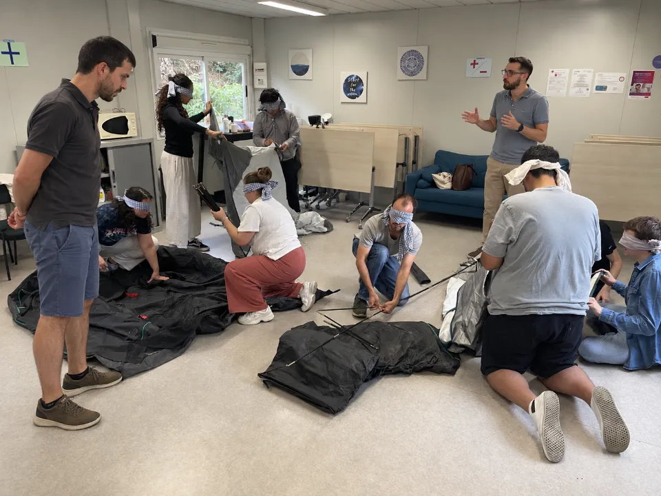Atelier Faire équipe : des participants aux yeux bandés montent une tente pendant que Stan et Stef les observent